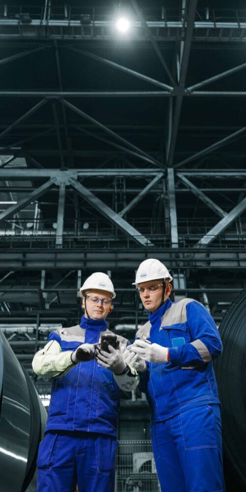 Two workers in hardhats and safety gear reviewing compliance documentation inside industrial manufacturing facility