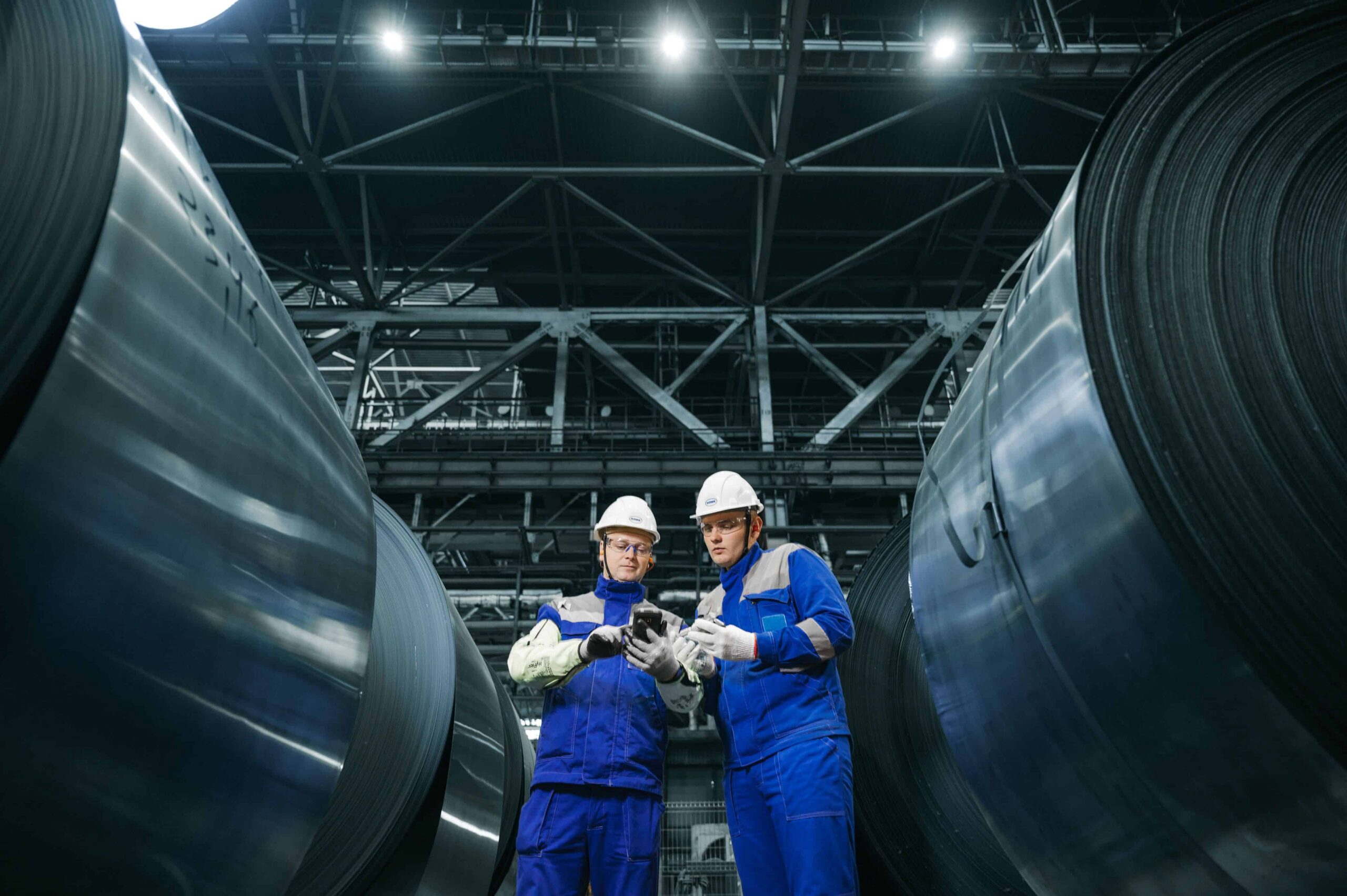 Two workers in hardhats and safety gear reviewing compliance documentation inside industrial manufacturing facility