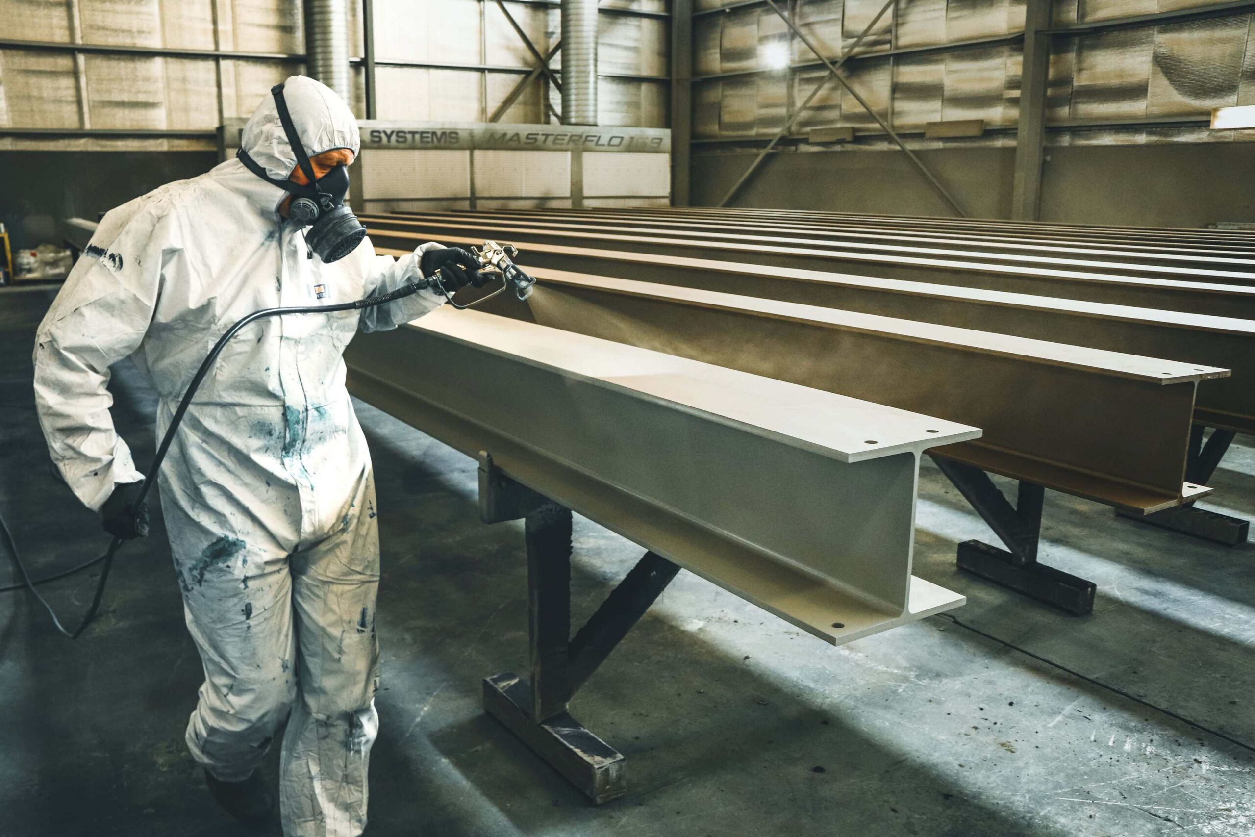 Steel fabrication shop worker applying protective coating to structural steel beams for industrial manufacturing project